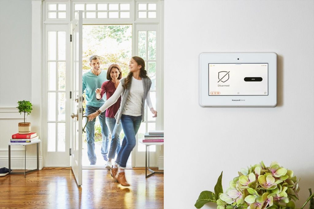 Family walking in the front door of their home past a security panel on the wall
